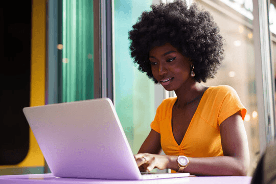 A woman with an afro hairstyle smiling while working on a laptop.